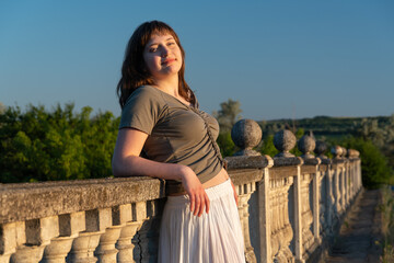 Naklejka premium Young woman leaning on stone balustrade during golden hour