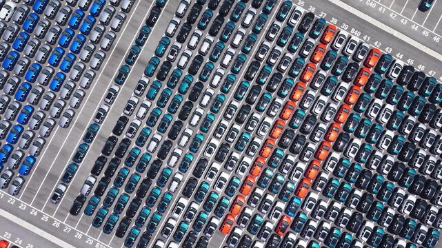 Aerial view of massive new car storage lot with neatly arranged multi-color sedans