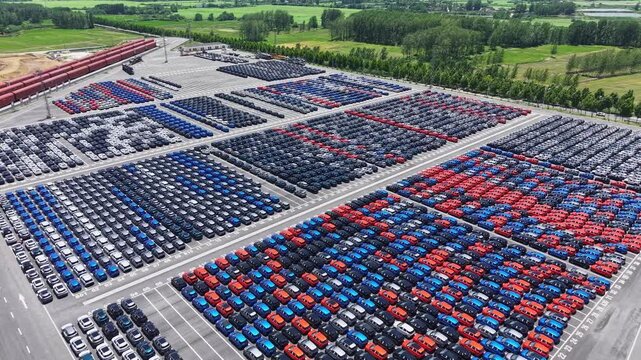 Aerial view of massive new car storage lot with neatly arranged multi-color sedans