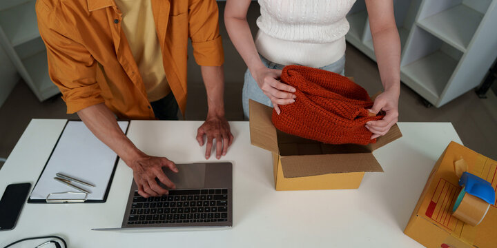 High angle view of cropped hands packing orange sweater into cardboard box for online retail shipping
