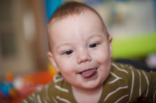 Charming mischievous grin of a precious baby peeking out a small tongue with bright, curious eyes in a warm, cozy home