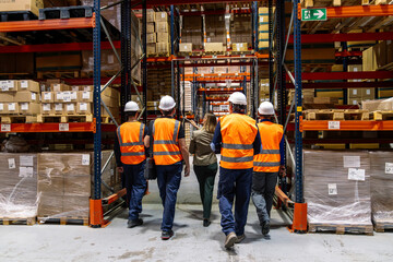 Fototapeta premium Group of workers and manager in safety vests and hard hats inspecting goods in a large storage and distribution center