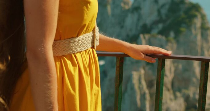 Relaxed woman tourist leaning on railing at Capri with scenic view of famous Faraglioni sea cliffs