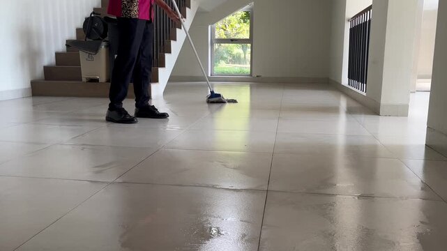 Professional cleaner diligently mopping a large, shiny tiled floor in a spacious modern home during deep cleaning process