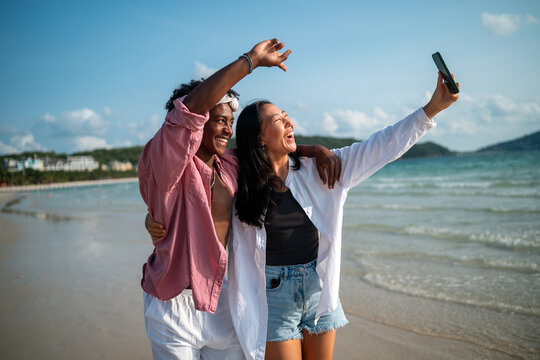 Trendy digital creator couple taking selfie by the beach, sharing travel content for social media