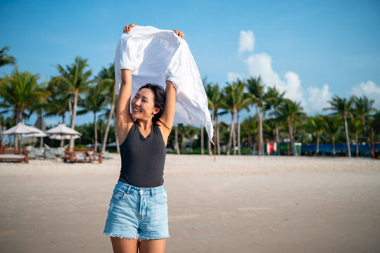 Happy woman celebrating freedom holding white shirt in the wind against blue sky at tropical beach