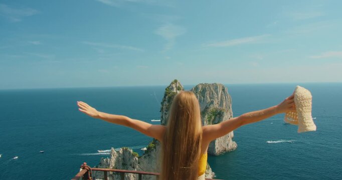 Woman on Capri cliff terrace overlooking iconic Faraglioni sea stacks on summer trip
