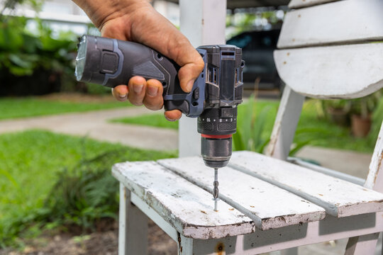 Cordless screwdriver driving a screw into chair wood.