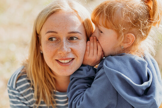 Daughter whispering secret in ear of mother