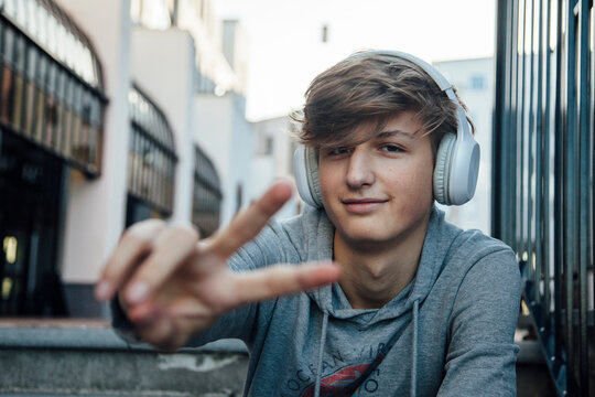Portrait of teenager with headphones showing victory sign