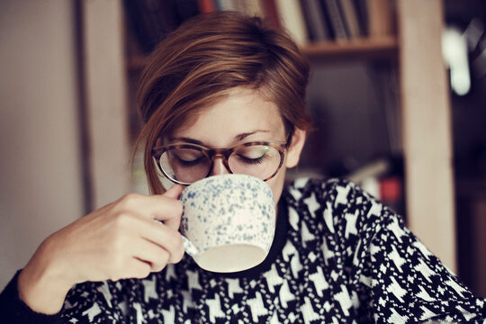 Woman in sweater drinks coffee indoors for morning relaxation