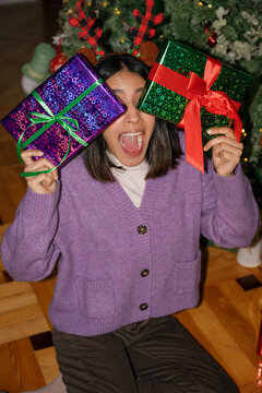 Excited woman holds a Christmas present over her face at home