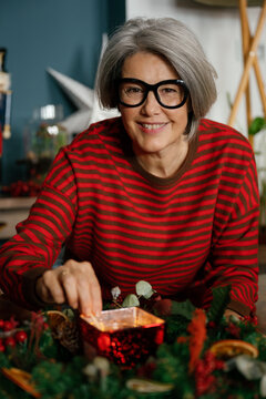 A smiling mature woman lights a candle in a Christmas wreath at home