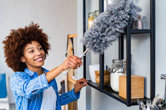 Smiling young woman cleaning rack in kitchen at home