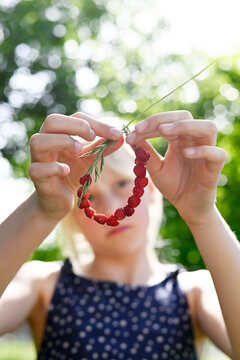 Blond girl holds a grass blade with strawberry in the garden