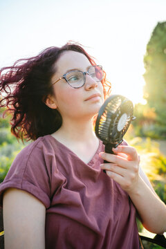 Teenage girl cooling down with a portable fan outdoors in summer