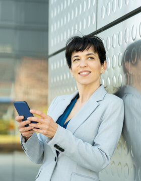 Female entrepreneur with mobile phone leaning on silver colored wall