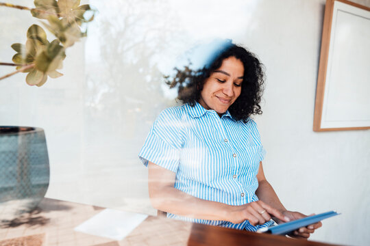 Smiling woman using tablet PC sitting by wall at cafe