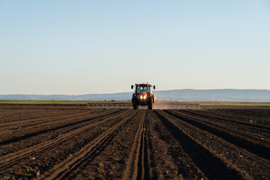Tractor spraying agricultural field with boom sprayer