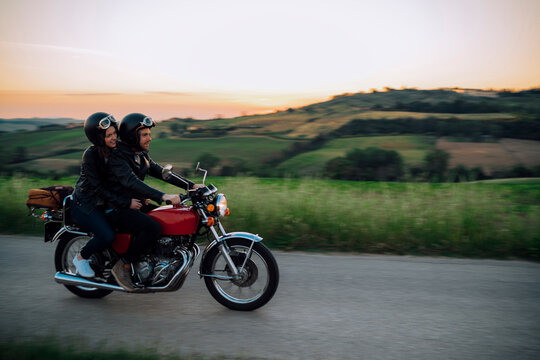 Young couple riding vintage motorbike on country road at sunset, Tuscany, Italy