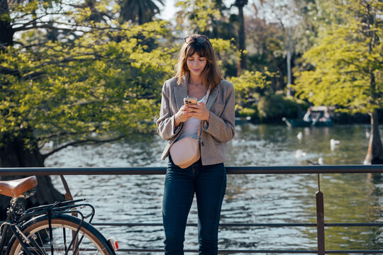 Woman using phone while standing by a lake in the park
