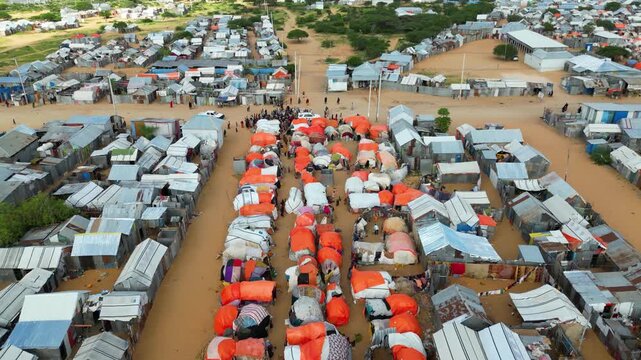 Moving high angle drone flight over a flooded humanitarian refugee camp in Somalia, highlighting rows of temporary shelters damaged by extreme weather and the urgent