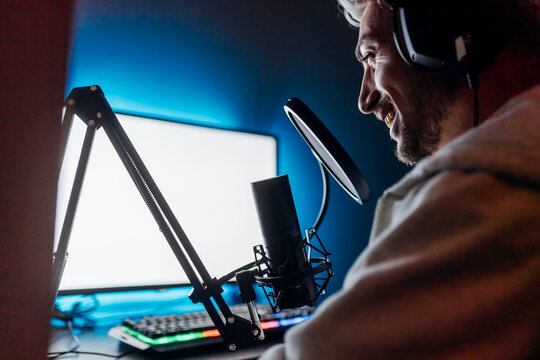 Smiling male gamer podcasting while playing game on computer at home