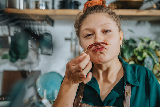 Playful chef making mustache with dry chili pepper while standing in kitchen