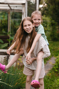 Girl giving her sister a piggyback ride in the summer garden