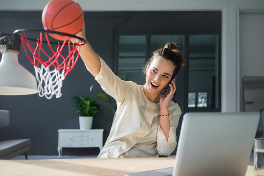 Portrait of freelancer on the phone throwing basketball into hoop at workspace