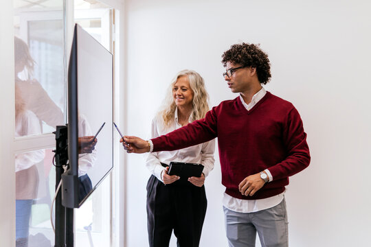 Young businessman explaining to colleague through presentation on screen at work place