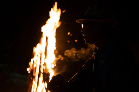Man plays guitar by a glowing bonfire on the beach at night