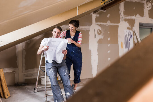 Young couple on construction site of their new home, looking at construction plan