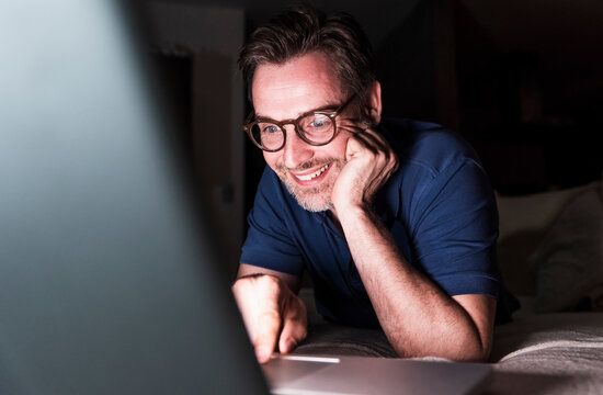 Portrait of smiling man lying on couch at home using laptop