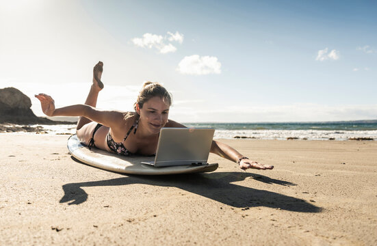 Young woman lying on surfboard, using laptop