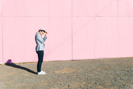 Young man in front of pink construction barrier, holding his hat