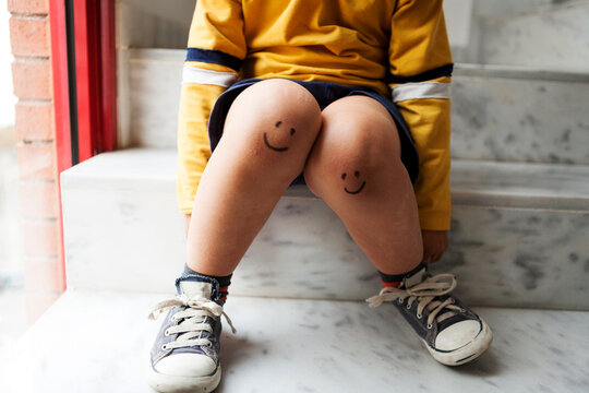 Boy sitting on stairs with smiley faces on his knees