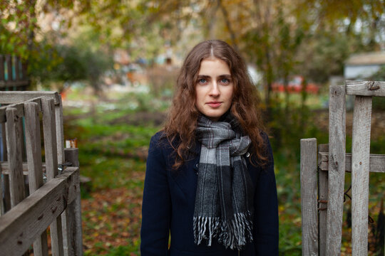 A cheerful young woman stands outdoors by a wooden fence in autumn