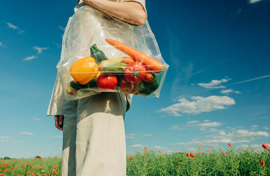 Woman holds transparent bag of organic produce in green field