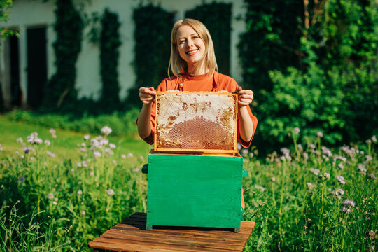 Female beekeeper holds a honeycomb frame above a green hive