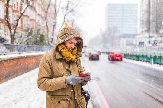 Young man standing next to the road in the city looking at cell phone