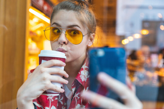 Young woman in a cafe taking a selfie while drinking a coffee