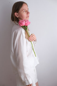 Model holding a pink peony flower wearing casual white clothing