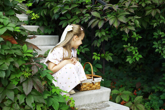 Young Girl in Floral Dress Sitting on Garden Staircase with Picnic Basket