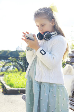 Girl with Smartphone and Headphones in Park: Technology and Childhood Adventure