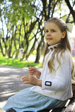 Smiling Girl with Dandelion in Sunny Park: Joyful Childhood Moment in Nature