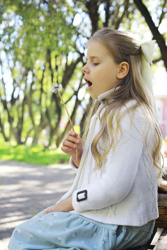 Young Girl Joyfully Blowing Dandelion Seeds Outdoors in a Park Setting