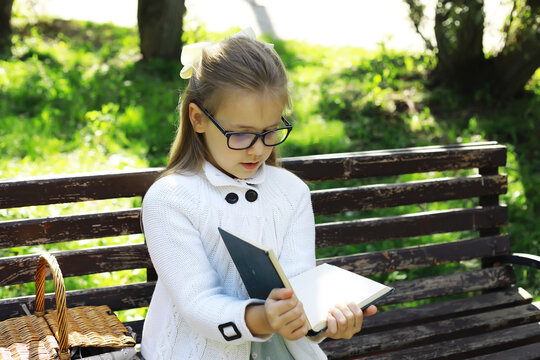 Young Girl in Glasses Reading Book on Park Bench Amidst Sunny Spring Day