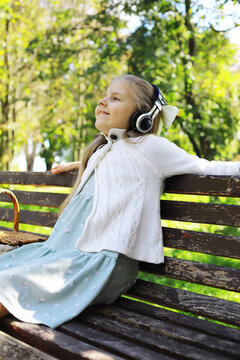 Joyful Girl Relaxing with Headphones on a Park Bench in Sunlit Garden Retreat