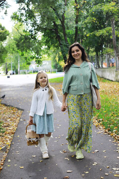 Mother and Daughter Strolling on Leaf-Covered Path in Autumn Park